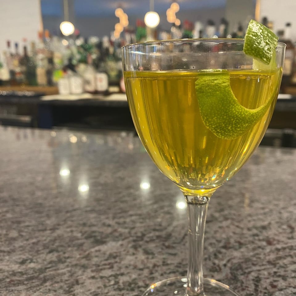 A yellow cocktail with a lime peel garnish sits on a speckled bar top at Redcrest Kitchen.