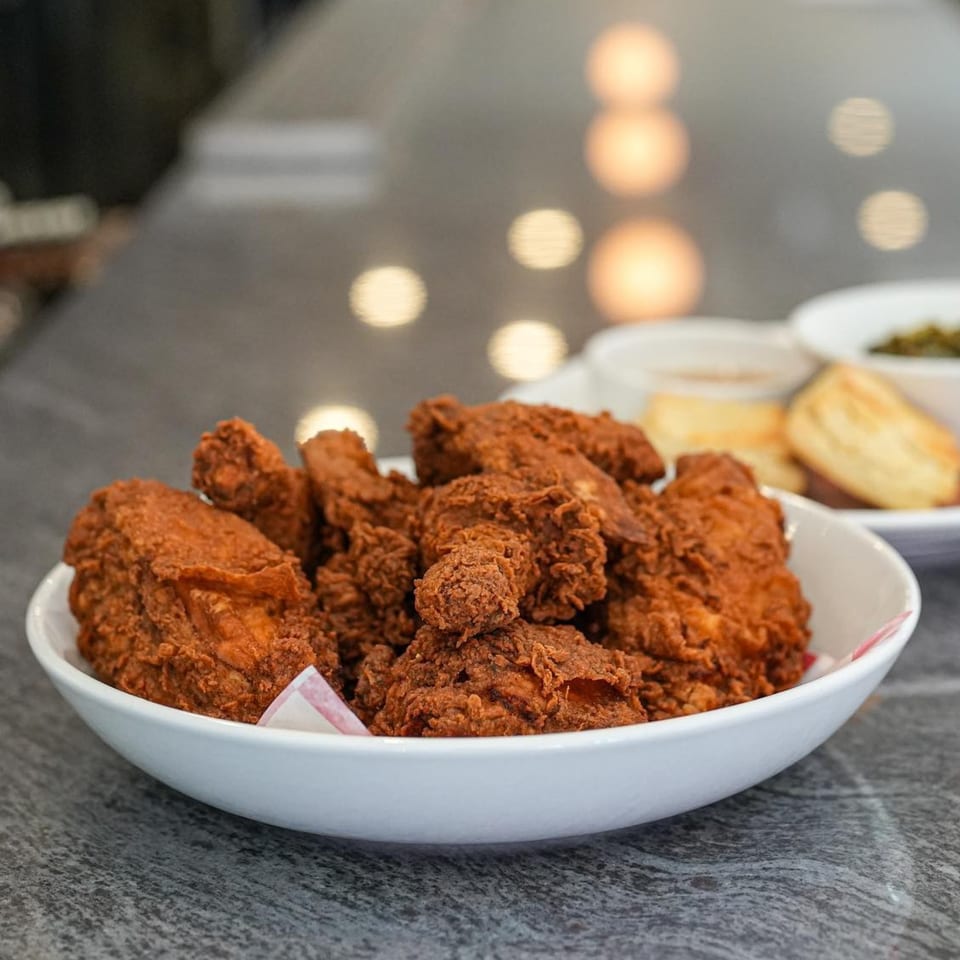 A white bowl filled with crispy fried chicken, with sides and biscuits blurred in the background.