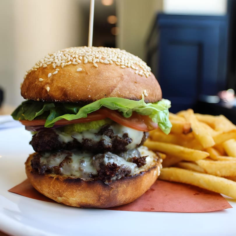 A Redcrest Kitchen double cheeseburger with lettuce, tomato, pickles, and fries on a white plate.