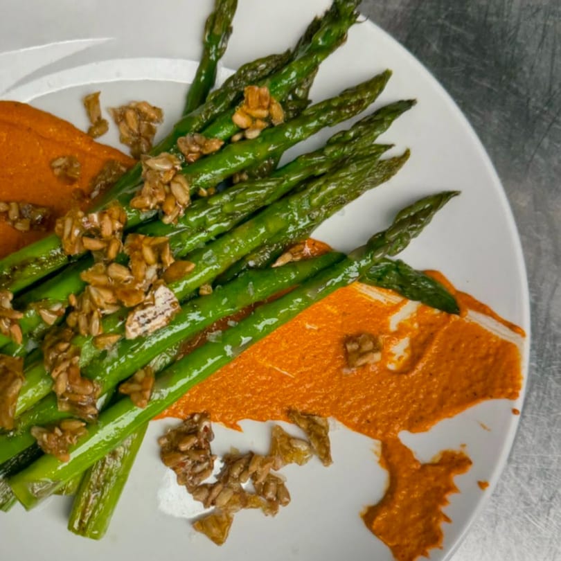 Bright green asparagus spears with a vibrant orange sauce and toasted seeds on a white plate.
